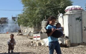 A young girl carries her brother through the Jurahiya settlement in Lebanon’s West Beqaa Valley. 